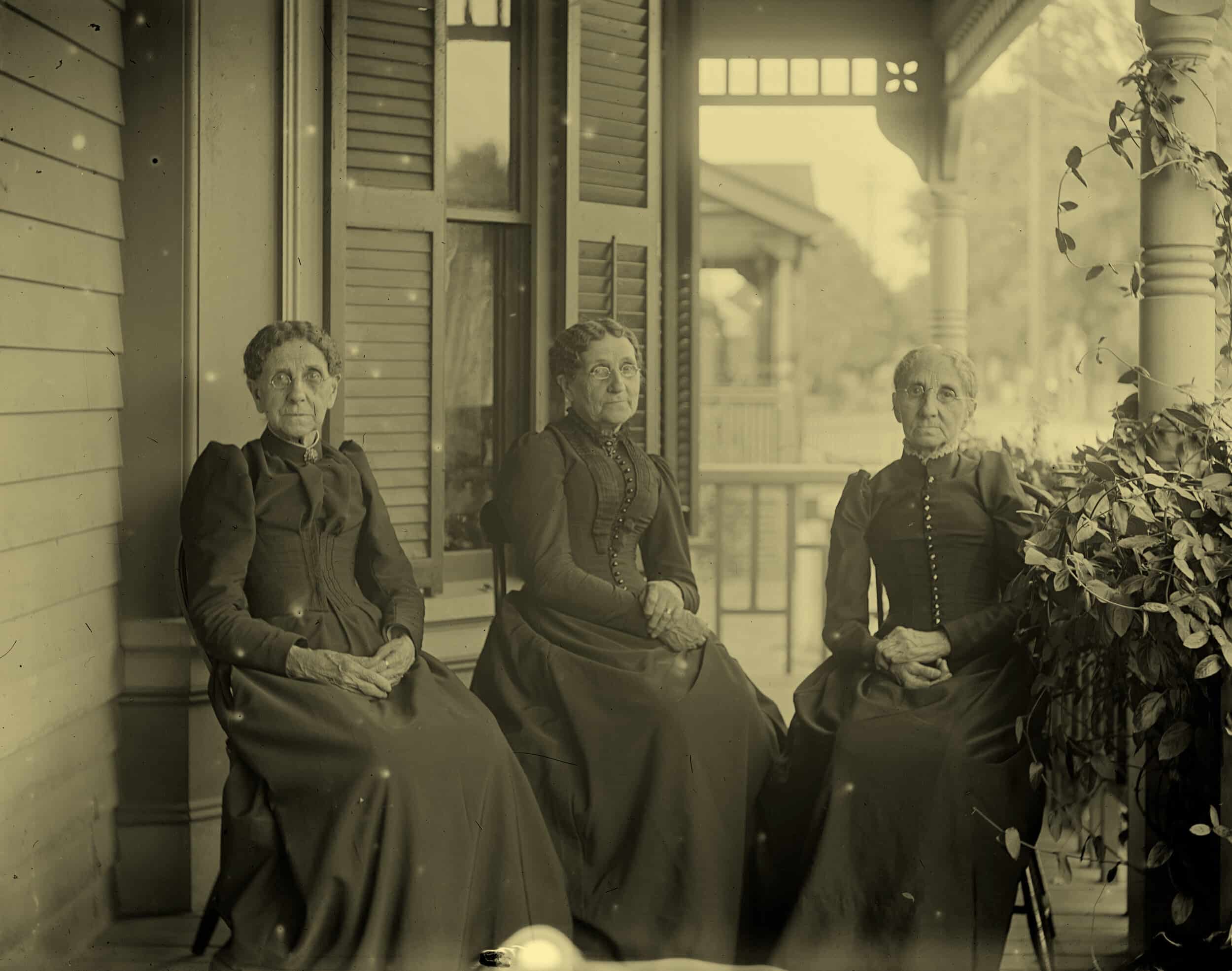 Three older women in a vintage photograph, sitting on a porch in nice dresses