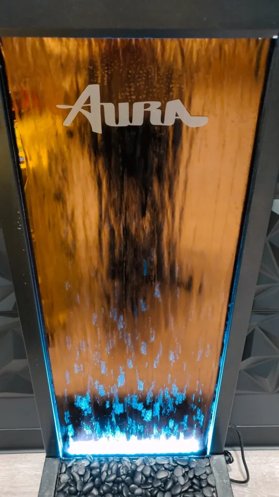 The glowing Aura water feature, framed by dark stone and blue light at Aura - Fall River.